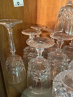 Multiple clear crystal wine and rocks glasses with diamond cut pattern resting upside down on a wooden shelf.