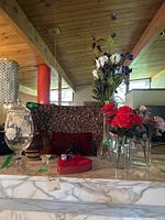 View of glass jar with lid, metal vase, woven rush tray, faux floral vases, whale carving, and candy box on marble surface under living room setting