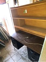 Desk with dark wood top and black drawer base, showing a white cable on the surface and tile floor underneath