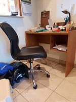 Desk and office chair positioned in a room near a window. The desk has visible stains and marks, chair has black cushioned seat and chrome base with caster wheels.