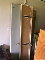 Two bifold closet doors leaning against wall: one white painted with knob, one unfinished with metal brackets visible