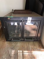 Front view of the black metal fireplace insert showing two glass sliding doors with metal handles and the top part with rusted metal.