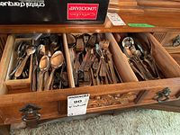 Top view of a wooden drawer organizer divided into three compartments containing mixed stainless steel spoons, forks, and knives, with a boxed set on top of the drawer.