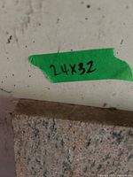 Close-up of slab marked “24x32” on green tape; light-colored marble slab front edge visible