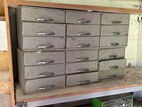 Front view of the nine-drawer grey metal cabinet showing silver handles and signs of wear.