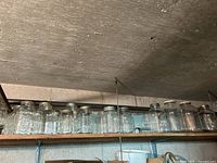Shelf of clear glass jars and containers in basement cold cellar, jars vary in size, all empty and arranged in a row.