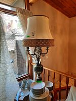 Full view of vintage ornate table lamp with cream fabric shade and metal base, showing its size next to dishes.