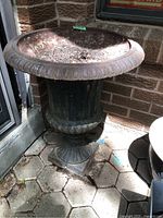 Side view of the iron planter showing shape, ornate base, and rust condition outdoors.