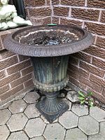 Iron planter positioned in a corner outdoors on stone pavers with visible rust and aging