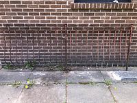 Photo of the full metal railing against a brick wall showing overall shape and rusting.