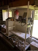 Full view of the white metal shelving unit with some various tools and containers on shelves (contents not included).