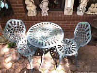 Photo showing full set of painted aluminum patio furniture including openwork round table and two chairs with worn painted finish.