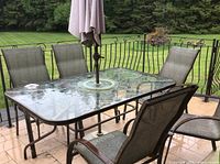 Overall view of patio set on deck showing six chairs around a glass-top table with patio umbrella and stand.
