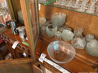 Varied pressed glass bowls, mugs, and espresso coffee pots on wooden shelves and table.