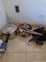 Overview of pressure cooker, pots, metal funnel, wooden spatula, and ladle on tiled floor