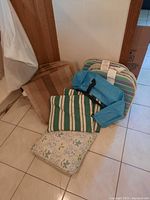 Photo of outdoor chair seats, backs, and three cushions stacked on the floor near a door, showing the pattern and condition of fabric items.