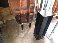 Photo of two vintage wooden side tables and a tall black CD stand inside a wooden framed room under construction or in storage, showing condition and overall shape.