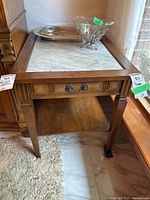 Full view of wood side table with rectangular inset white marble top, drawer, and lower shelf. Shows wood grain, drawer handle, and side legs.