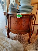 Front view of wood side table with curved front door, floral wood inlay, marble inset top, and dishes on top.