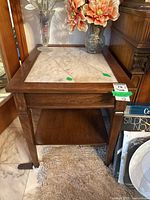 Front view of the wood side table with white marble inset top showing the two cracks marked with green tape and decorations on top.