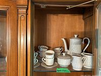 Full tea set displayed inside a cabinet with various pieces including teapot, cups, saucers, creamer, and sugar bowl.