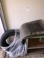 Shows tire stacked with car mats on top in a garage or storage area