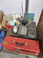 Overview of assorted tools, electrical supplies, drill bits in containers, and a red metal toolbox with a latch and handle