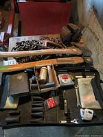 Wide photo showing various tools on a table including hammers, chains, a vice, and smaller tools