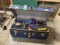Opened blue vintage trunk displaying organized office supplies in multiple compartments.