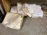 Image showing folded linens and blankets in white and cream tones with lace and embroidery, some still in packaging and placed on floor