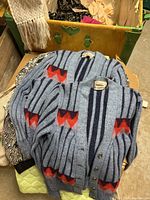 Two gray cardigans with red and black geometric pattern laid over a yellow storage container