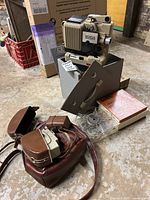 Overall view of the vintage Agfa movie camera on a box, clear plastic film reel, movie tote, light meter, and additional accessories arranged on the floor.