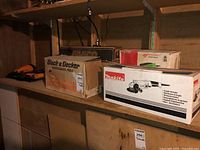 Three boxes of power tools on basement shelves, including Black & Decker and Makita boxes displaying product images and branding.