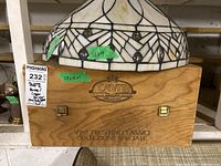 Photo of stained glass lamp shade placed on top of wooden wine storage box with engraved Cavit branding and dimensions label.