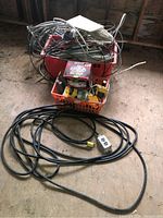 Full view of lot showing wiring bundles in orange plastic basket, light fixture parts in red container, and extension cord coiled on floor