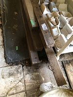 Three long wood beams resting on the floor with visible wear and surface marks, alongside white ceramic items on shelving.