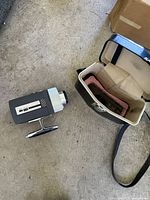 Bell & Howell Autoload Super 8 movie camera next to open carrying case with foam insert.