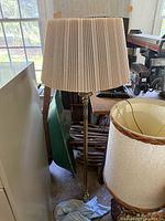 Full view of the brass floor lamp with pleated beige shade in a storage area.