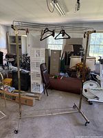 Full view of the tall brass étagère with several hangers, set in a cluttered room.