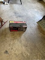 Box of Craftsman belt sander on a concrete floor, showing front and sides of the packaging with product information and images.