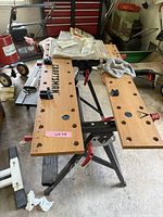 Full view of craftsman workbench showing two wooden panels with holes, black plastic clamps, red clamp levers and metal legs with support structure