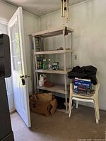 Photo of a 5-tier gray shelving unit against a wall next to a door, with some items on shelves and around but contents not included.
