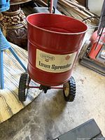 Red Ortho lawn spreader showing front view with label on bucket and wheels.