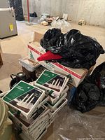 Photo of stacked boxes including artificial Christmas tree box and multiple boxed twenty-three-light window candelabras with white candles; some black garbage bags and other containers are visible around.