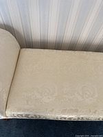Close-up of cream damask fabric upholstery showing subtle floral pattern and sheen on the bench seating surface.