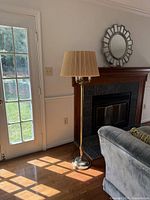 Full height view of the brass floor lamp next to a door and near a fireplace, showing the full lamp with shade and base on a hardwood floor.