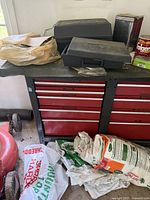 Red metal tool cabinet with black frame, 9 drawers. Black cases and plastic bags on top.