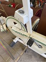Close-up photo of vintage Tunturi exercise bike showing white frame, green stripe, brand name, pedal, and speedometer device.