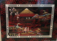 Front cover of vintage Asian scrapbook featuring detailed scene of Mount Fuji, traditional figures, bridge, and floral accents in red, black, and gold colors.