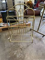 Vintage brass plated rack with arched top, horizontal and vertical bars, metal base for storage, on concrete floor in a room with furniture.